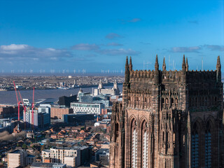 Fototapeta premium Aerial sunrise view of Liverpool shows Liverpool Cathedral, Royal Liver Building, Albert Dock museums, red cranes, modern blocks, and offshore wind turbines.