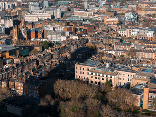 Naklejka premium Aerial sunrise over central Liverpool, UK, shows St. Luke's Church tower, brick terraces, modern apartments, institutional blocks, and winter bare trees with long shadows.