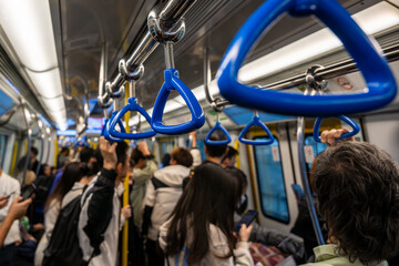 Crowded subway train with passengers standing under blue handles during rush hour. Urban public transport concept showing mobility, density, daily commute and city lifestyle