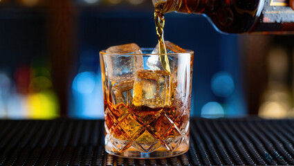 Pouring amber whiskey into crystal glass with ice cubes