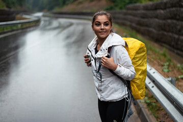 Young woman with a yellow backpack standing on a wet road in the rain