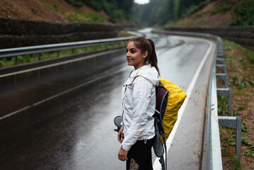 Young woman with backpack standing on a wet road in the rain