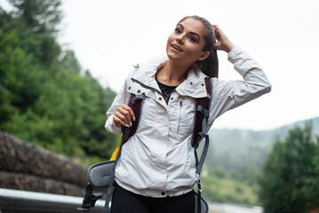 Young woman hiker with backpack pauses on a misty mountain road, touching her hair