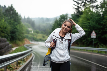 Young woman with backpack walking on a wet mountain road in the rain