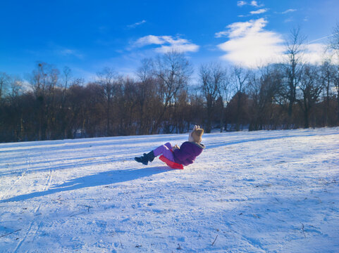 Joyful Child Sliding Down Snowy Hill in Normafa Hungary Under a Bright Blue Sky