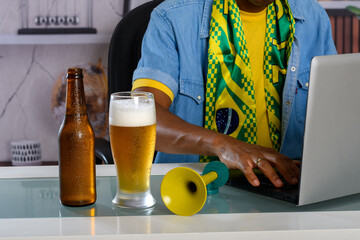 A Brazilian soccer fan enjoying a beer and using his laptop at the table during the match.