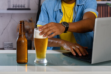 A man enjoying a beer while working on his laptop.