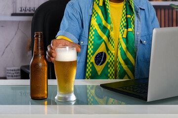 Brazilian fan enjoying beer and using a laptop at the table.