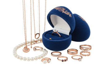 White pearls, rose gold jewelry, and engagement ring spilling from a blue egg box, presented in a velvet box on a white background, concept of opulent luxury.