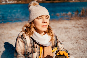 Woman closing eyes while sitting by lake, breathing fresh air, mindful pause, stress relief and...