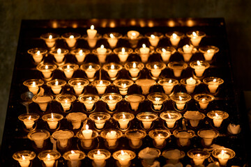 Rows of burning white votive candles in glass holders casting a