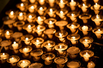 Rows of burning white votive candles in glass holders casting a