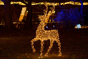 Golden glowing reindeer Christmas light decoration amidst shadowy trees during a nighttime holiday l