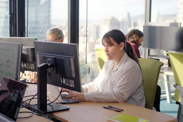 Young caucasian woman manager works at her laptop in a bright corporate office with city views, focused on typing and analysis during a productive workday in a modern workspace.