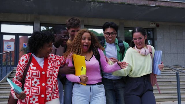 Happy group of multiethnic students gathering together after class, posing and smiling looking at the camera on the university campus celebrating end of lessons and enjoying community and friendship