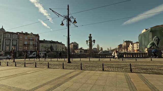 Timelapse of Lions Bridge in Sofia, Bulgaria, on a sunny day, showing stone pillars, street lamps, cobblestone pavement, pedestrians, lion statues, and surrounding historic buildings, BG, 01 Jan. 2026