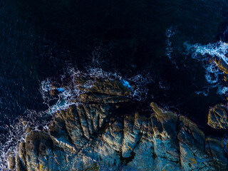 Dark water surrounds rocky coastline with waves crashing against shore at sunset
