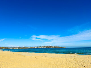 Wide view of a sandy beach with clear water and blue sky near a coastal town during daytime