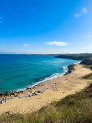 Coastline view with rocky shore and clear water under blue sky at midday near a coastal town