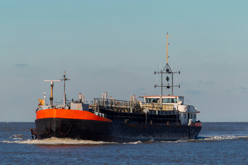 Fototapeta premium Work barge with orange hull navigating water during evening light