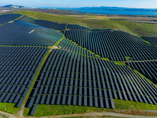 Solar panels cover a large area on a hillside near a body of water, showcasing renewable energy infrastructure under a clear sky during the day