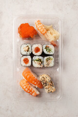 Assorted sushi rolls and nigiri in plastic takeout container

