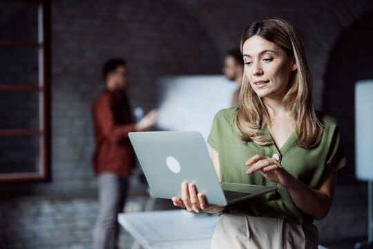 Focused businesswoman using digital technology with a diverse team behind her - Powered by Adobe