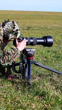 Camouflaged nature photographer alertly scanning horizon for elusive flying birds with patience