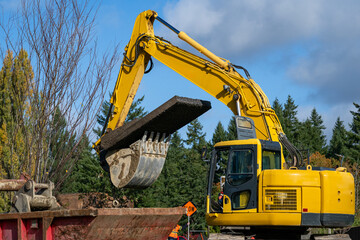 Excavator bucket attachment moving section of asphalt cut out of road to dig a utilities trench, public infrastructure construction site
