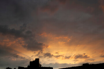 Moody dramatic sunset with orange and gray storm clouds over urban building skyline