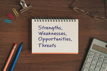 There is notebook with the word strengths, weaknesses, opportunities, threats. It is as an eye-catching image.