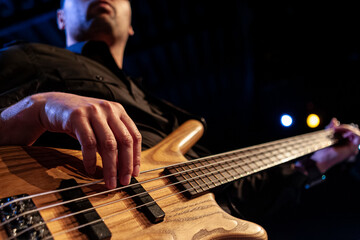 Bassist playing wooden bass guitar on stage with dramatic blue stage lighting
