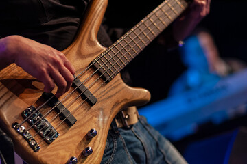 Fototapeta premium Close-up of bassist playing natural wood grain bass guitar during live performance
