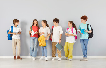 Group of diverse students, including teenagers and children, standing on a grey background, engaged in conversation. They are pupils in a school setting, focused on education and learning.