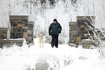 man and dog in winter walking over a stone bridge