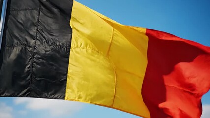 The vibrant national flag of Belgium proudly waves in the gentle breeze against a clear blue sky symbolizing the rich history unity and independence of the European nation a powerful emblem of patrio.