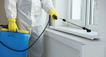 Pest control worker in protective suit spraying insecticide indoors, closeup
