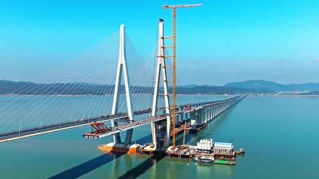 Aerial shot of modern cable-stayed bridge under construction with giant tower and crane over the sea in Ningbo, China.