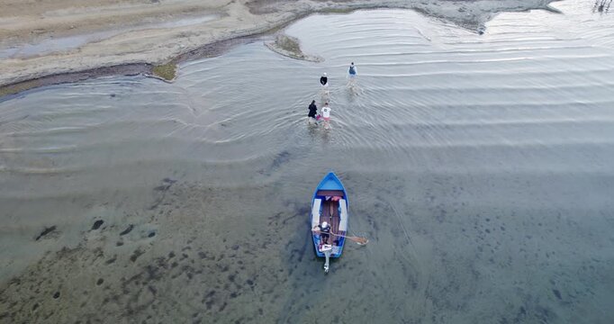 Tourist people disembarking off small motorboat on arrival at tropical island, aerial cinematic shot