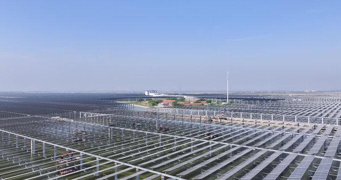 aerial video of a large-scale solar-aquaculture hybrid project under construction, panels rising over tidal flats with active crews and clean-energy infrastructure.