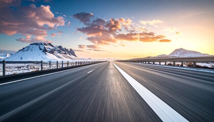 A scenic, long highway stretches towards the horizon under a vibrant sunset, flanked by snow-capped mountains and a guardrail