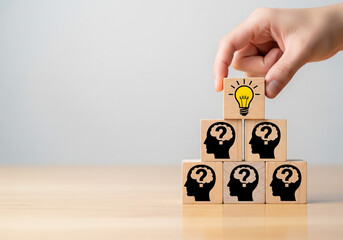 Hand placing a wooden block with a light bulb icon on top of blocks with question mark heads representing finding a solution and creative thinking.