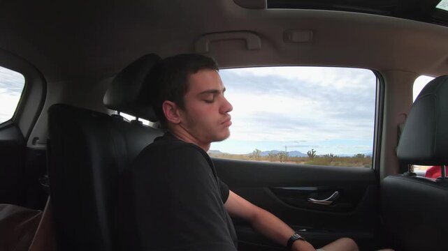 Tired male passenger sleeping in the backseat of a car. Car is driving through the Nevada desert. Tired man resting in the car while on his USA road trip with friends