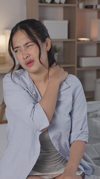Stressed Asian woman suffering bad neck muscle ache sitting bed feeling unhappy exhausted face hurt from office syndrome health problem tension strain discomfort overworked home bedroom Vertical