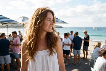 Smiling woman with long wavy hair standing at a busy seaside cafe with ocean view