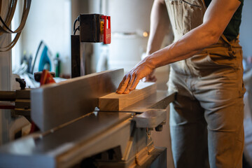 Woodworker work on electric planer saw, trimming wood pieces. Excess cutting, surface leveling,...