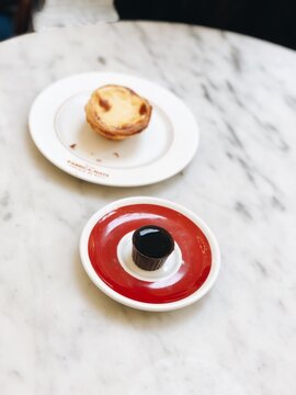 Traditional Portuguese Pastel de Nata Dessert and Ginjinha/ Ginja Cherry Liqueur in Chocolate Cup on Marble Caf&eacute; Table in Lisbon, Portugal