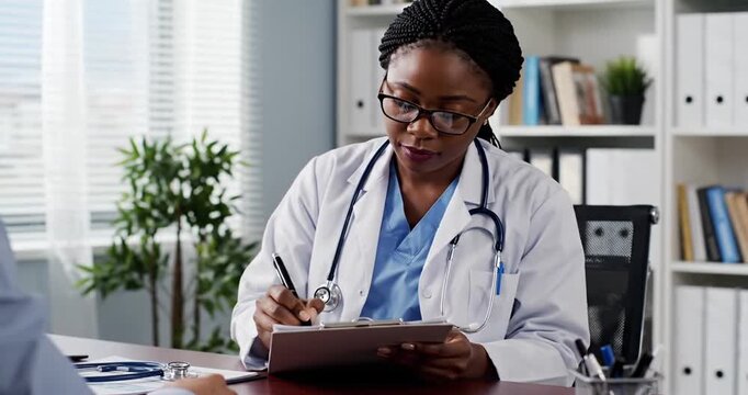 Female doctor in a modern office taking notes while consulting a patient, plants in background
