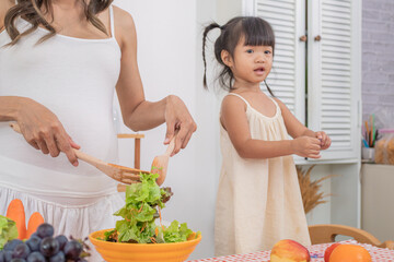 Asian healthy pregnant mother and children lifestyle bonding togetherness, pregnancy woman cutting tomatoes with naughty little daughter, motherhood family happy activities together in kitchen