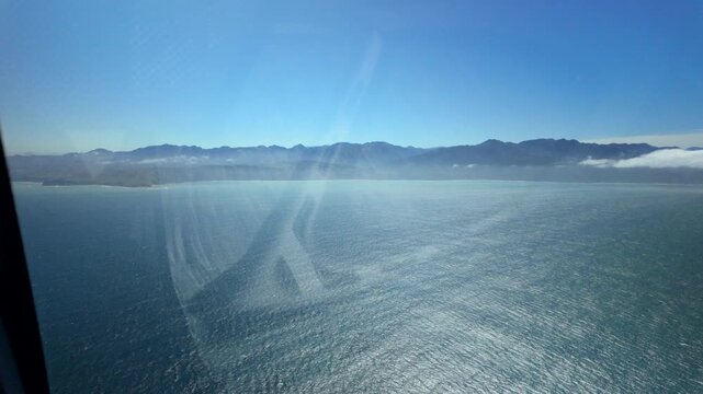Helicopter window view of sparkling sea and mountain range